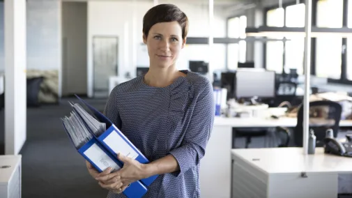 Frau steht mit Akten im Arm im Büro Frau steht mit Akten im Arm im Büro
