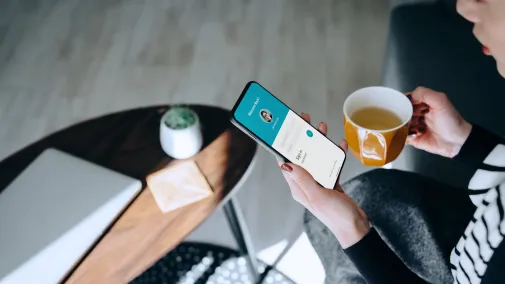 Frau sitzt mit Smartphone und Tasse am Tisch Frau sitzt mit Smartphone und Tasse am Tisch